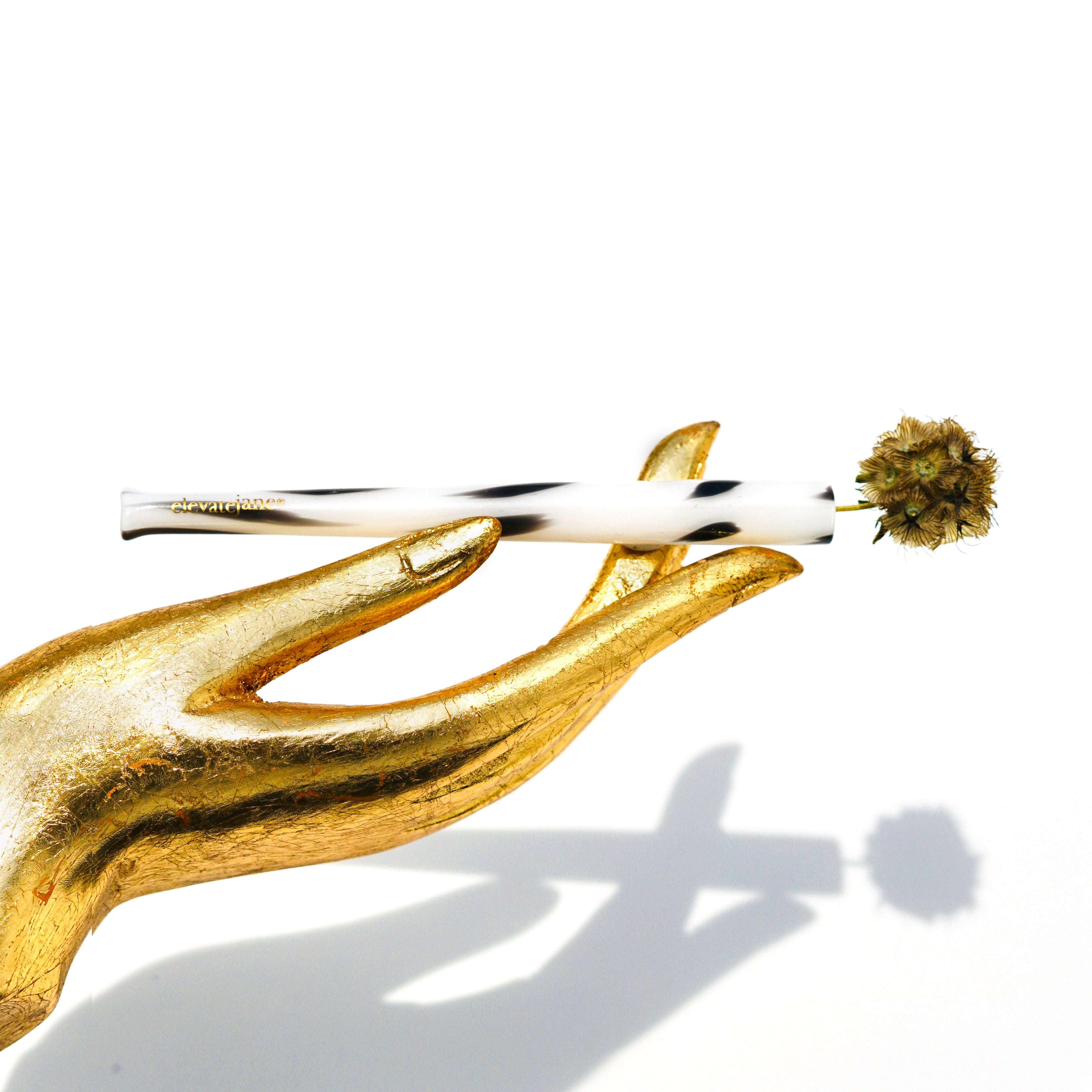 Gold hand statue holding a Cruella joint holder made from mixed black opaque glass spots on white opaque glass