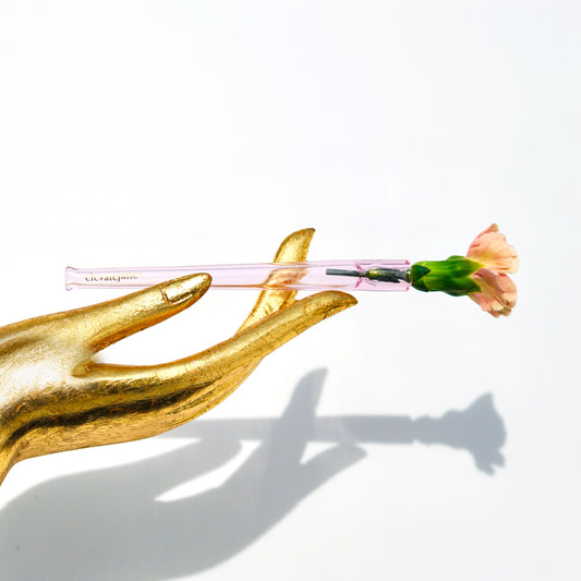 Gold hand statue holding a Cruella joint holder made from transparent pink glass