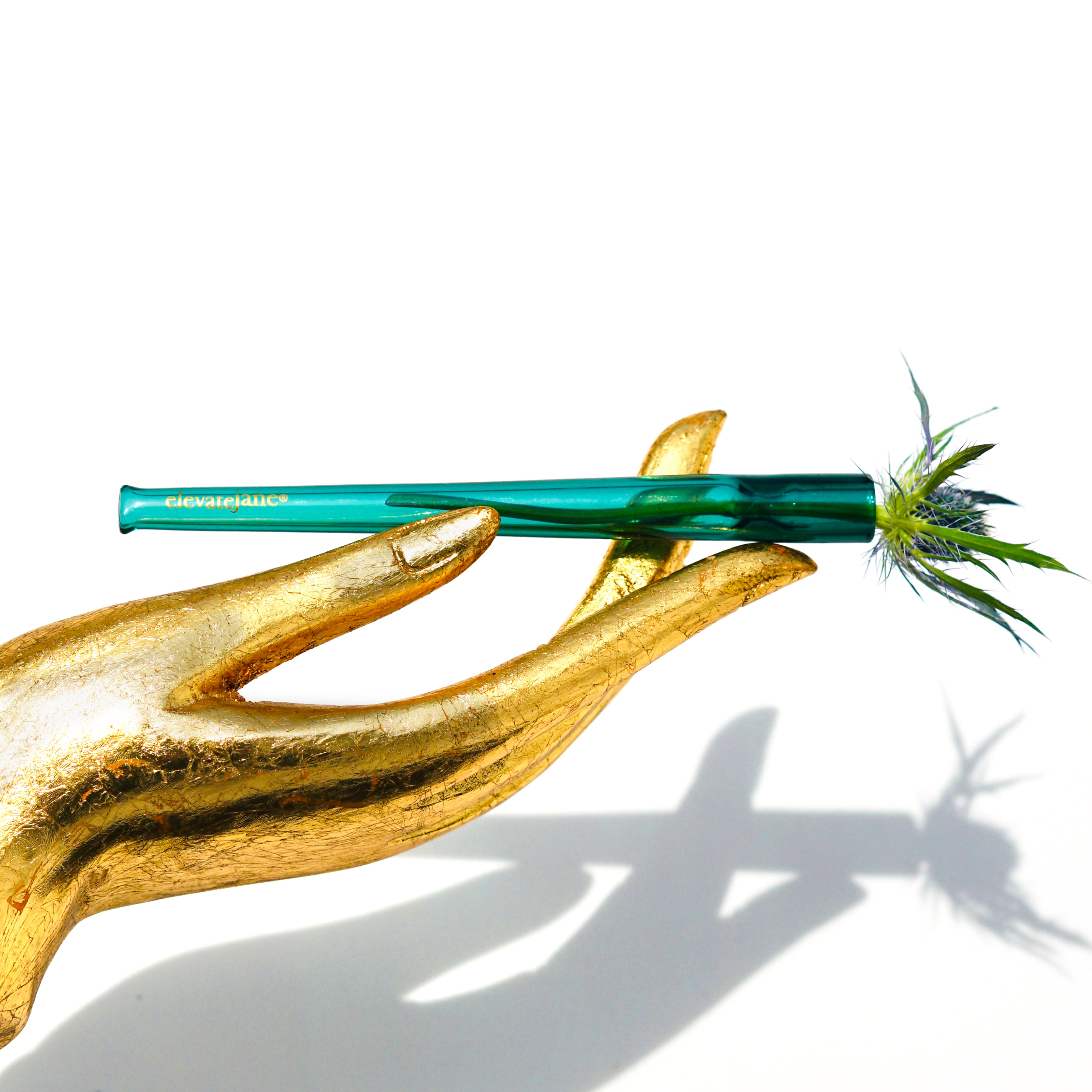 Gold hand statue holding a Cruella joint holder made from transparent teal glass