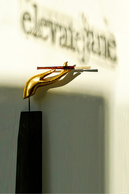 Gold hand statue holding a Cruella joint holder made from amber and black glass in a tortoise shell print