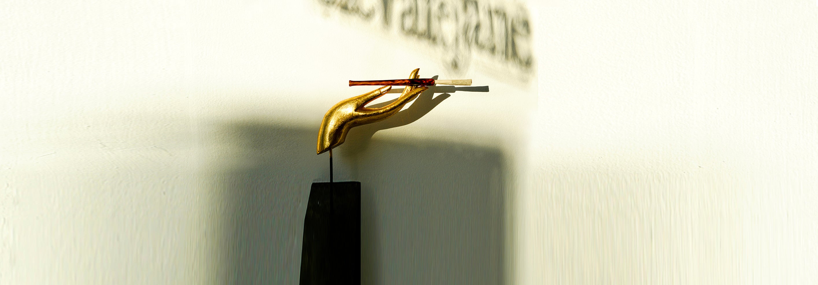 Gold hand statue holding a Cruella joint holder made from amber and black glass in a tortoise shell print