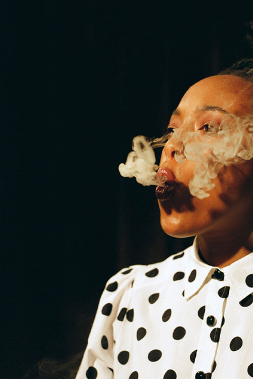 Woman in black and white shirt blowing smoke rings against a black background